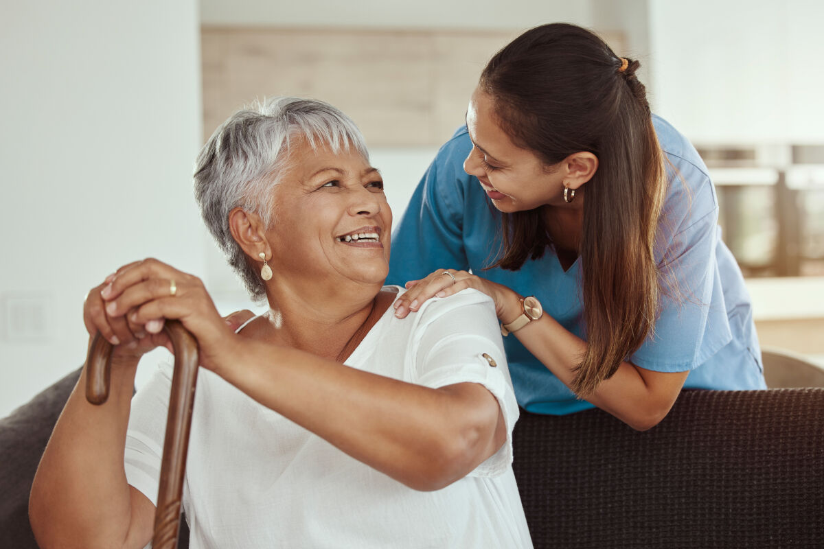 Seniorin und Pflegerin lächeln sich an, während sie zu Hause gemeinsam Zeit verbringen.